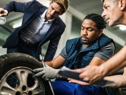 African American mechanic and his coworker repairing a tire of customer's car at auto repair shop.